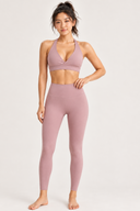 A woman modeling a matching MOXII MOUVE mauve pink activewear set consisting of a wrap-style sports bra and high-waisted leggings, photographed against a clean light grey studio background.